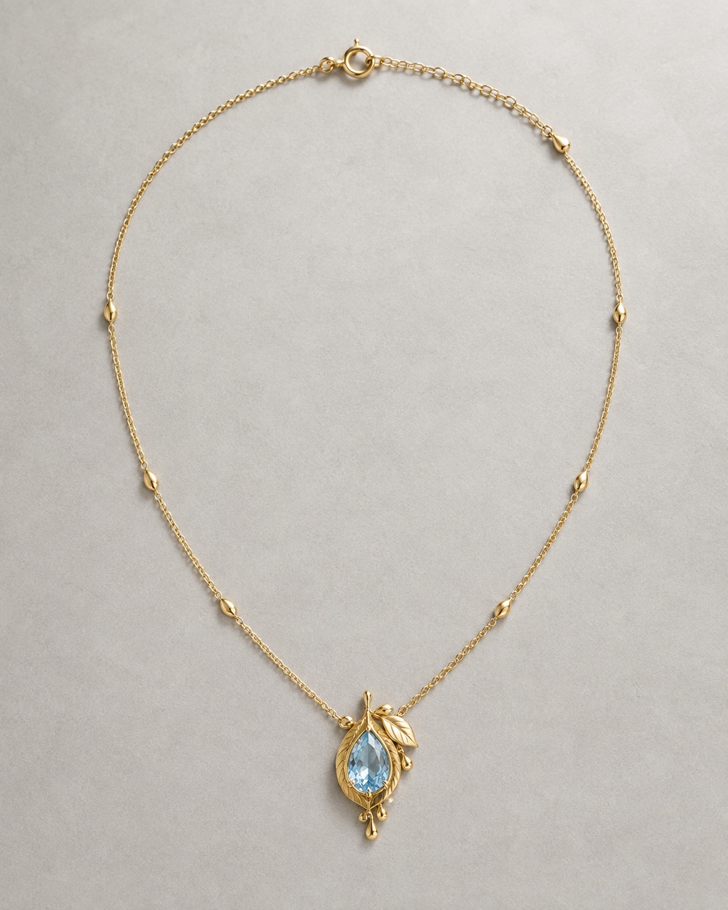 Botanical yellow-gold necklace concept with a pale blue sapphire pendant